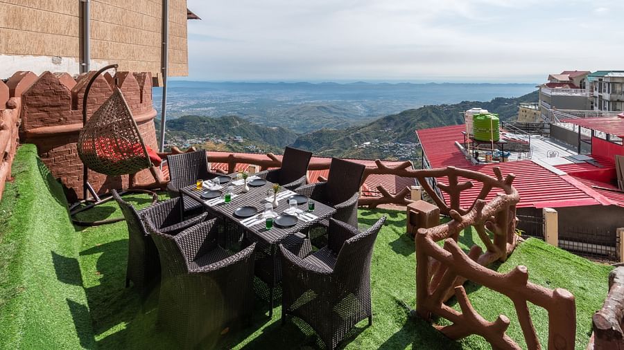 An outdoor dining area with a table and chairs set on a grassy terrace overlooking a scenic mountain landscape | DLS The Pearl